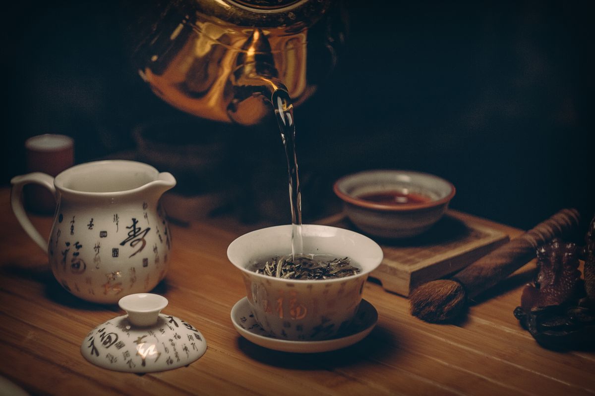 Freshly poured coffee in a cream ceramic cup next to roasted beans.